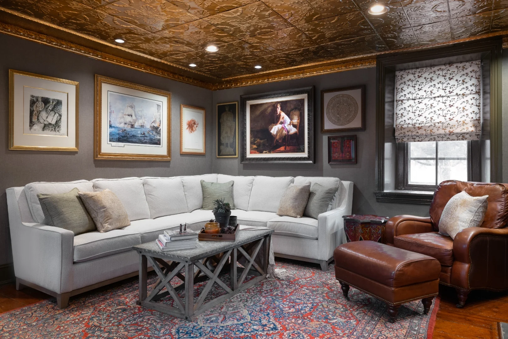 Gray-walled seating area with a white sectional, layered art collection, antique Persian rug, and the cherry built-ins and stone fireplace in the Bucks County living room