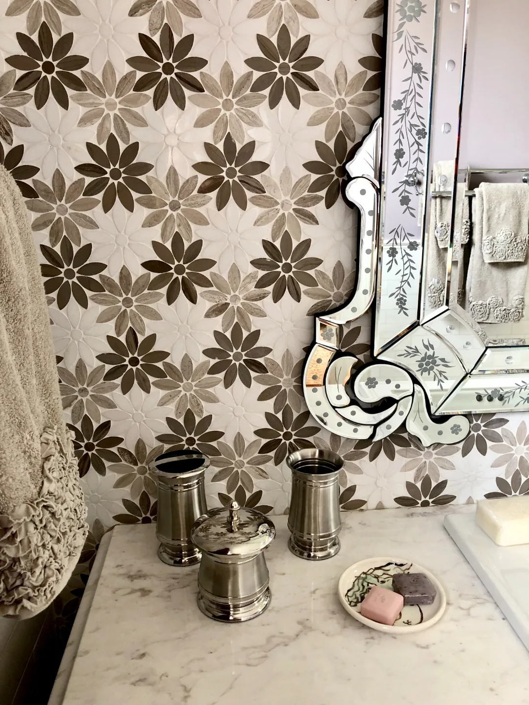 Detail of the floral marble mosaic feature wall, ornate Venetian mirror, and polished-nickel canisters on the marble vanity top in the Cape May ensuite bathroom