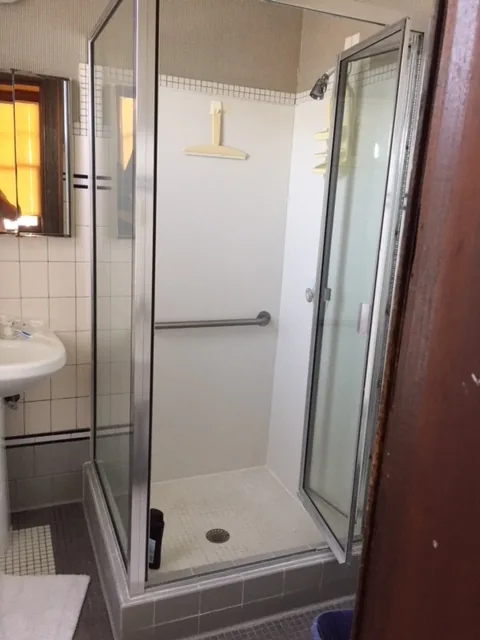 Cape May bathroom before renovation with a dated framed corner shower stall and a builder-grade glass enclosure