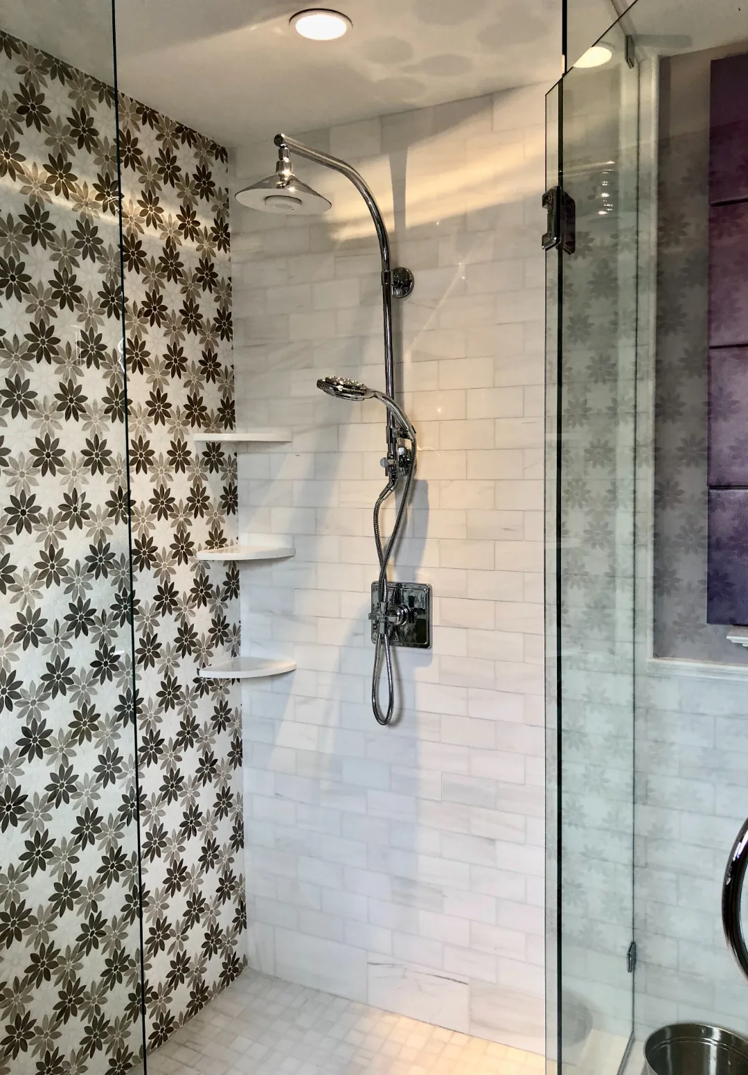 Interior of the Cape May ensuite shower with a polished chrome rain head, handheld sprayer, floral marble mosaic, and marble subway tile