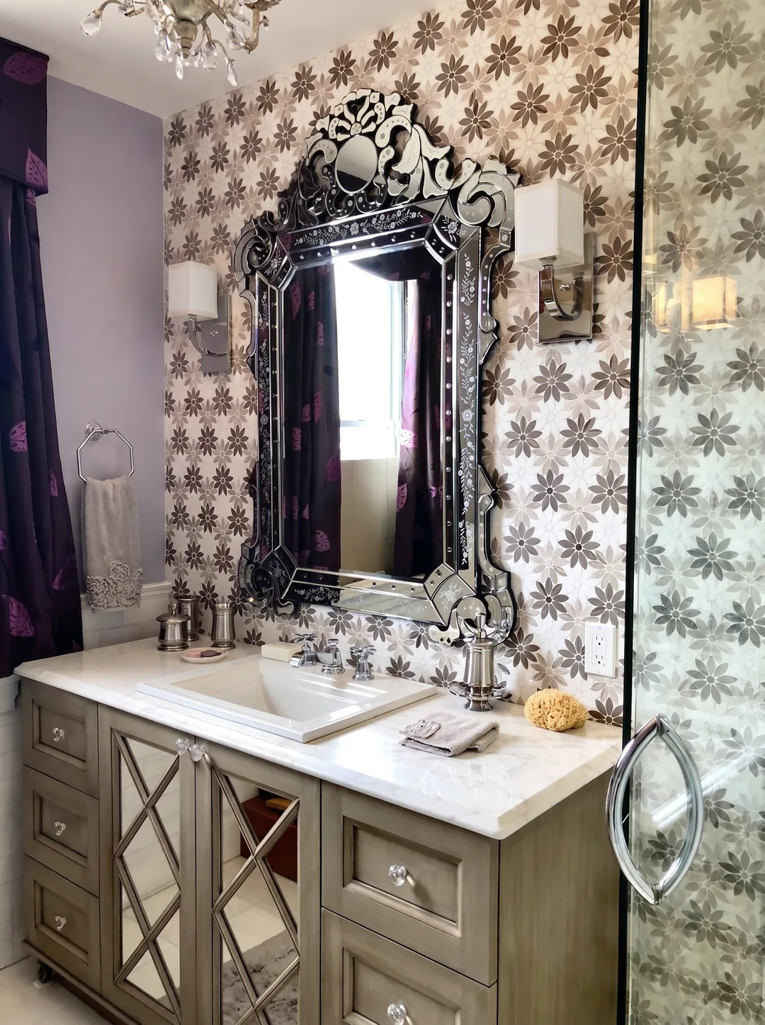 Angled view of the Cape May ensuite bathroom vanity showing the mirrored cabinetry, Venetian mirror, polished-nickel sconces, and floral marble mosaic wall