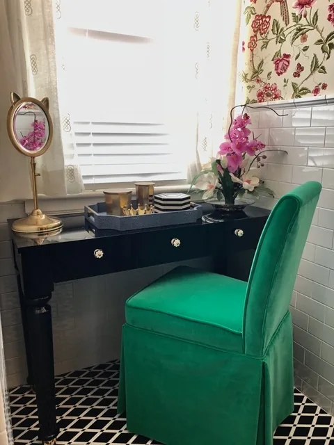 Black lacquer makeup table with a green velvet skirted chair, brass cat-ear mirror, shagreen tray, and pink orchid beneath a white-curtained window in the Cape May chinoiserie bathroom
