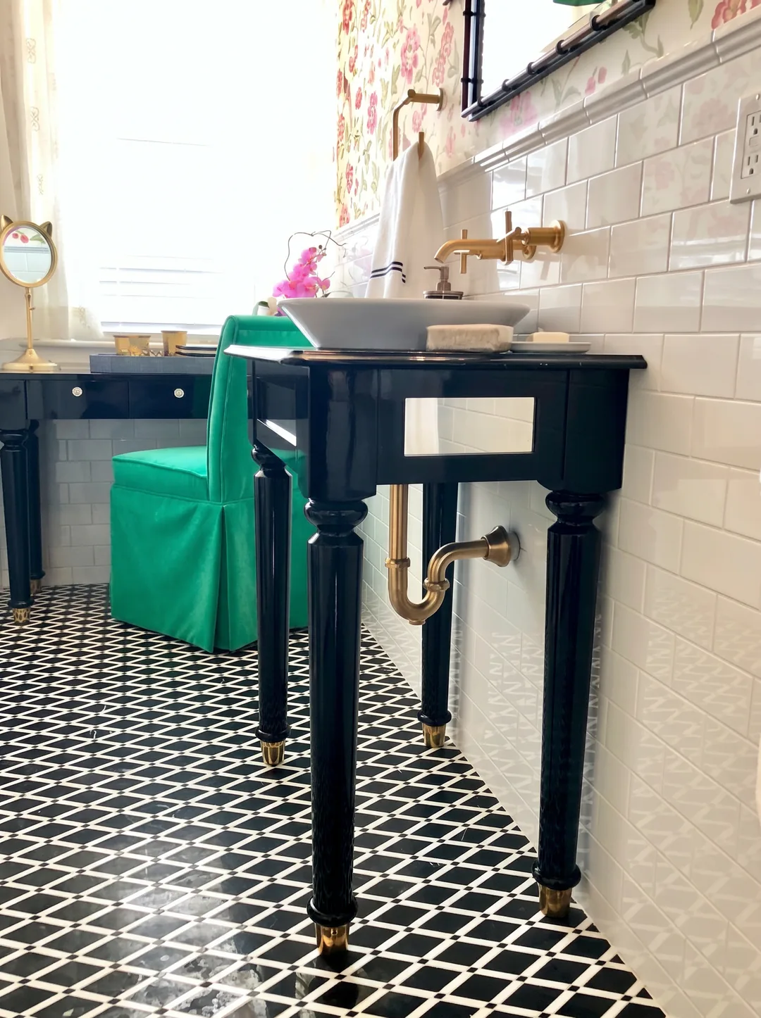 Side profile of the black lacquer console vanity with turned legs, brass feet, exposed brass P-trap, vessel sink, and green velvet chair over the black-and-white geometric floor in the Cape May chinoiserie bathroom