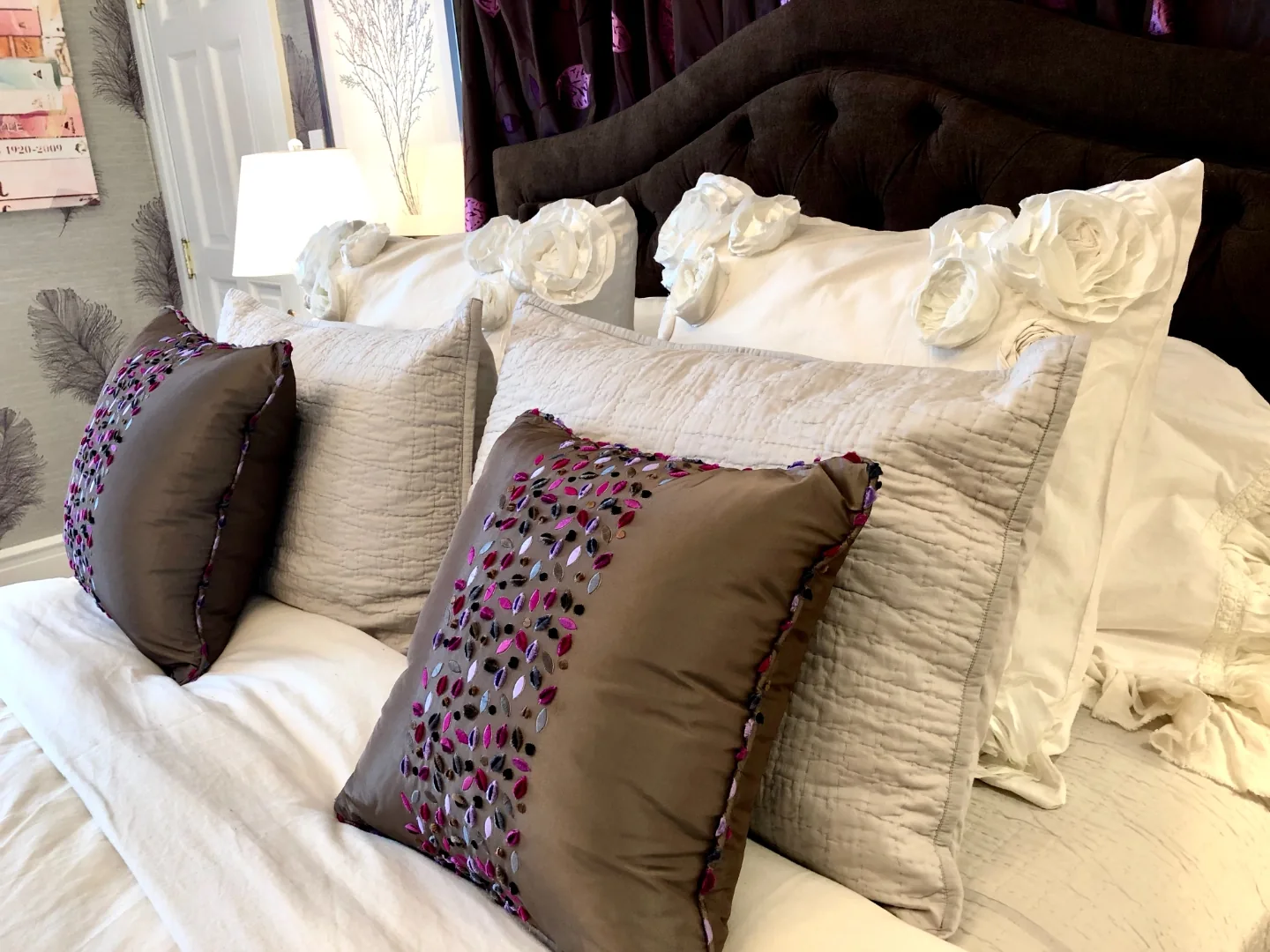 Layered bedding detail with rosette shams and embellished accent pillows against a tufted velvet headboard in the Cape May ensuite