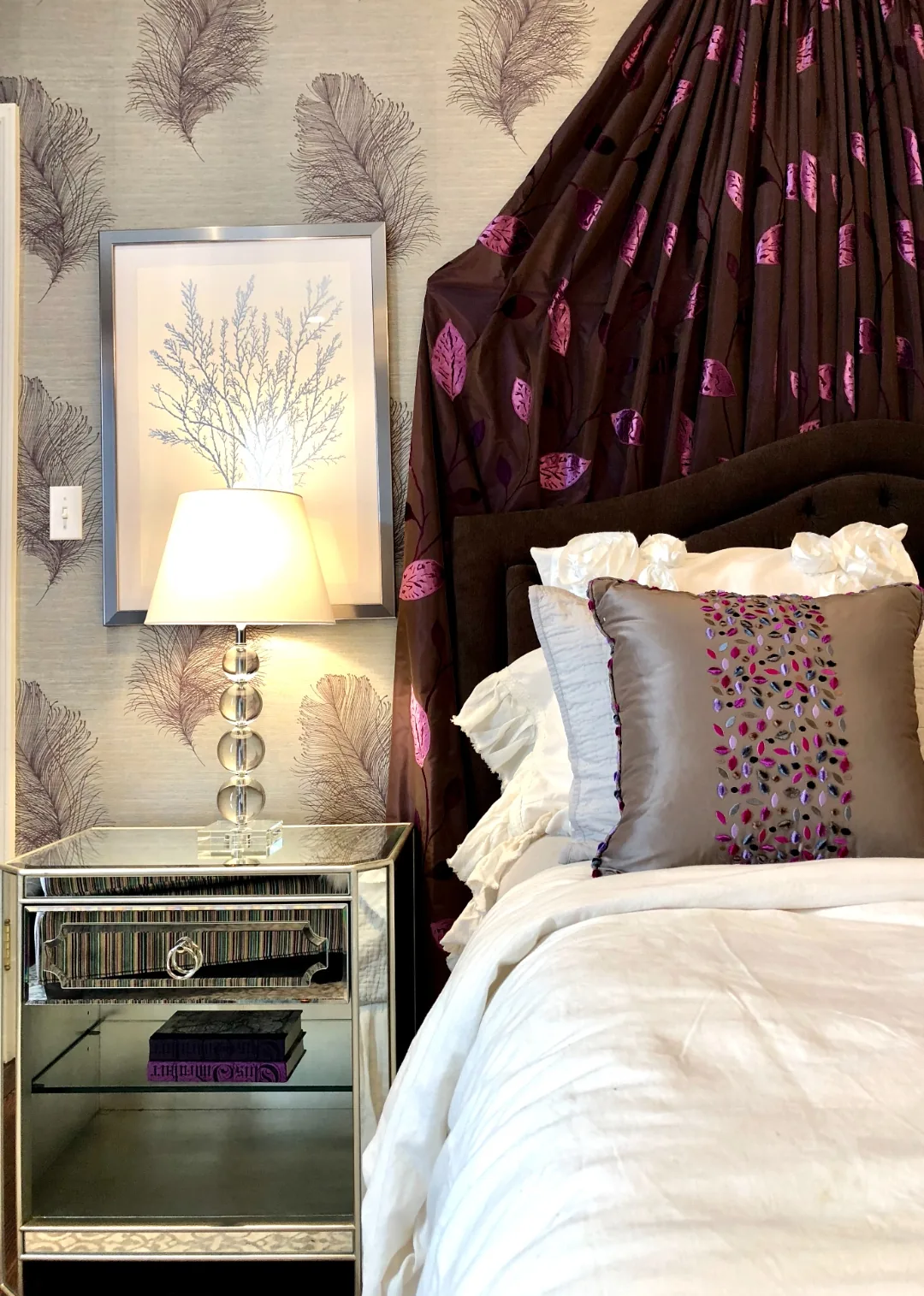 Detail of a mirrored nightstand with a crystal lamp, framed botanical print, and the plum draped bed crown in the Cape May ensuite