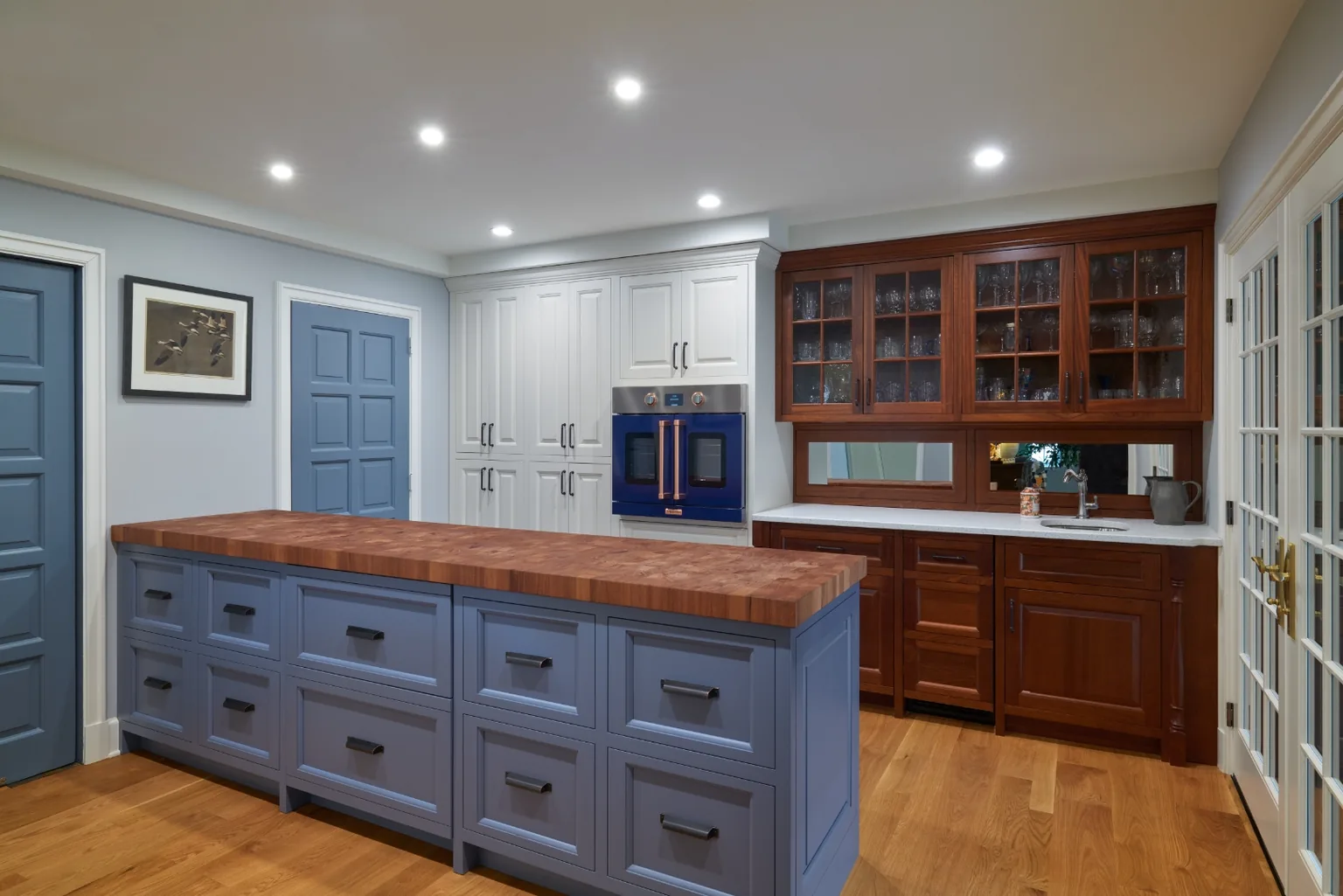 Beverage bar area with a periwinkle butcher-block island, cherry glass cabinetry, and French doors opening to the patio