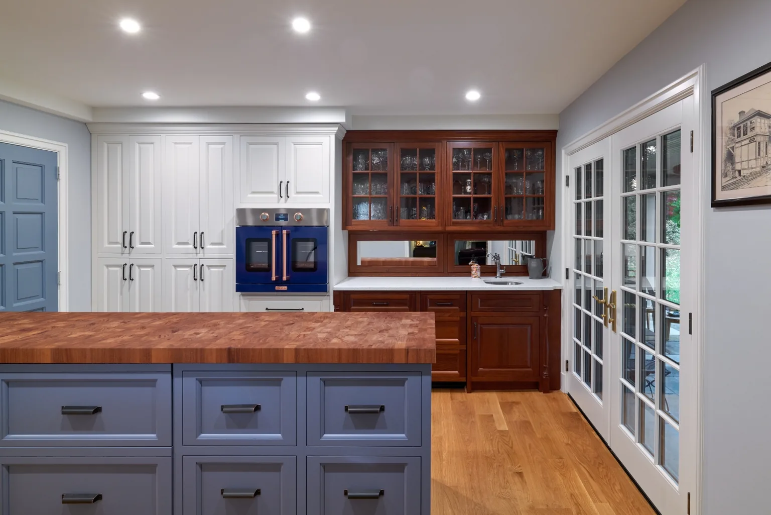 Beverage bar with a cobalt blue French-door wall oven, copper trim, cherry glass-front cabinets, and a periwinkle island