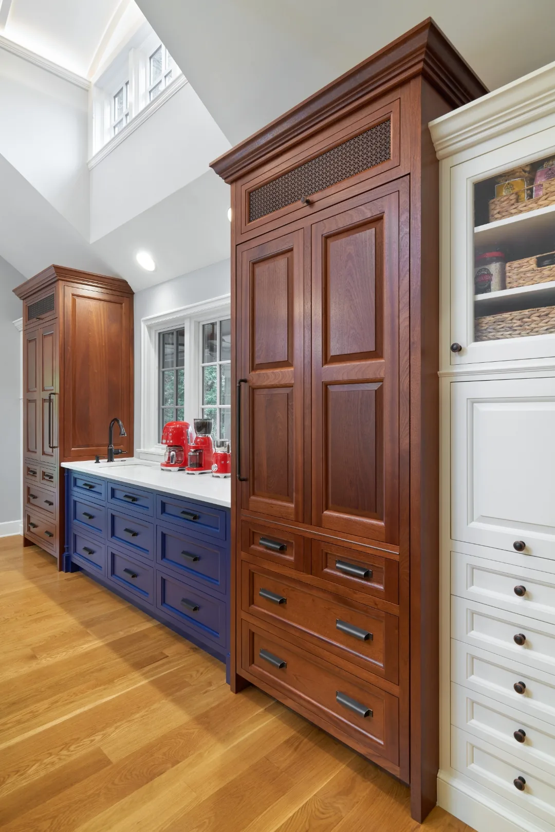 Navy blue cabinetry with white countertops, cherry pantry towers, and red enameled appliances in a Chester, PA kitchen
