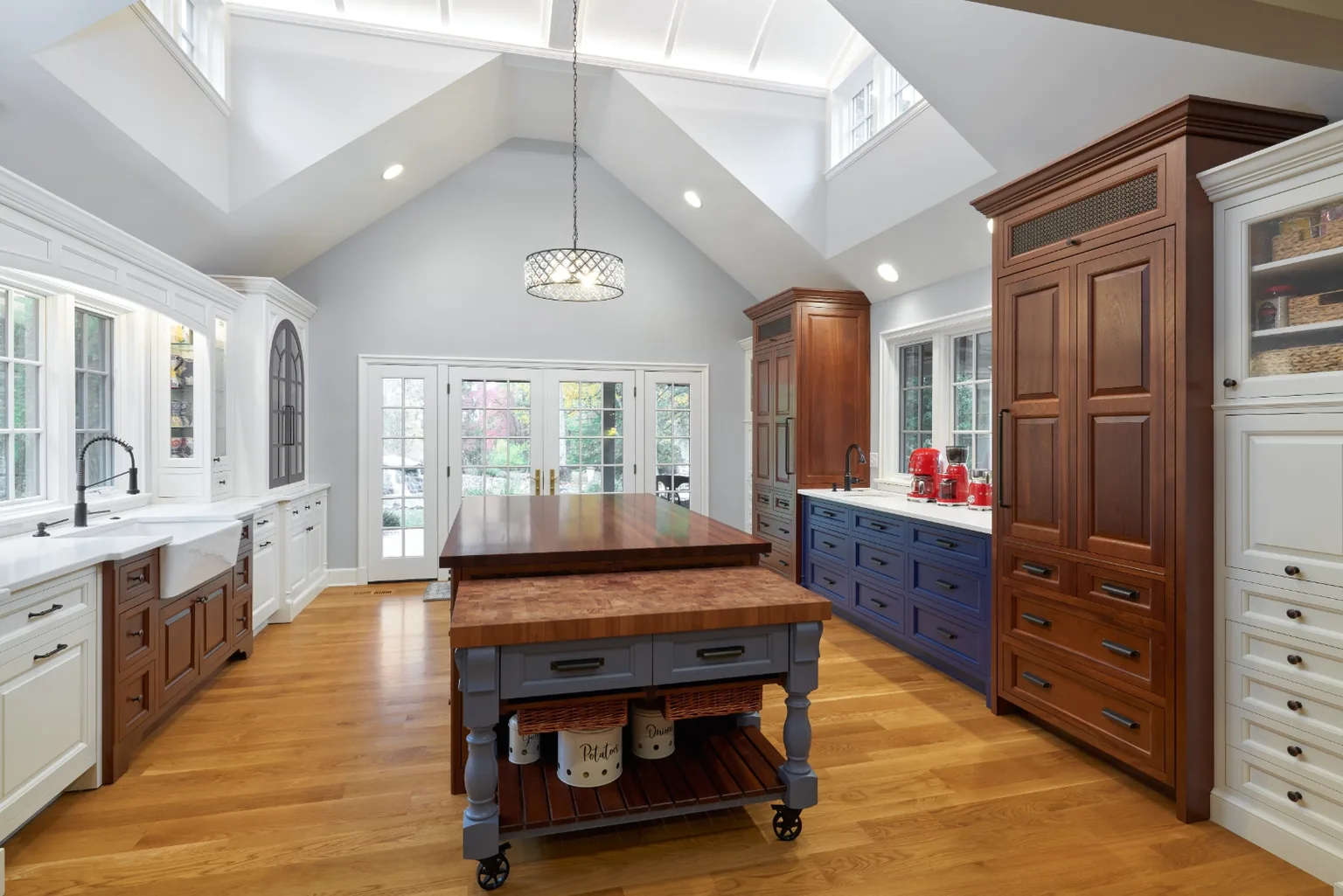 Vaulted Chester kitchen with twin butcher-block work islands, cream and cherry cabinetry, and a paneled refrigerator tower