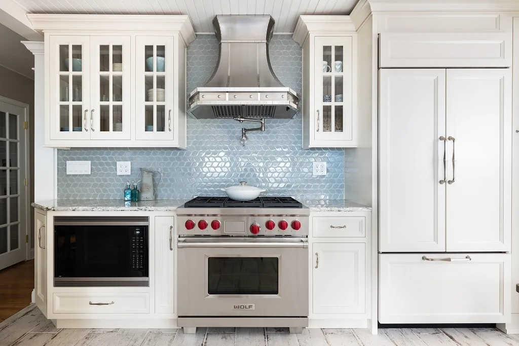Churchville kitchen appliance wall with a stainless Wolf range and curved hood, blue hexagon glass tile, glass-front upper cabinets, a panel-ready refrigerator, and marble counters