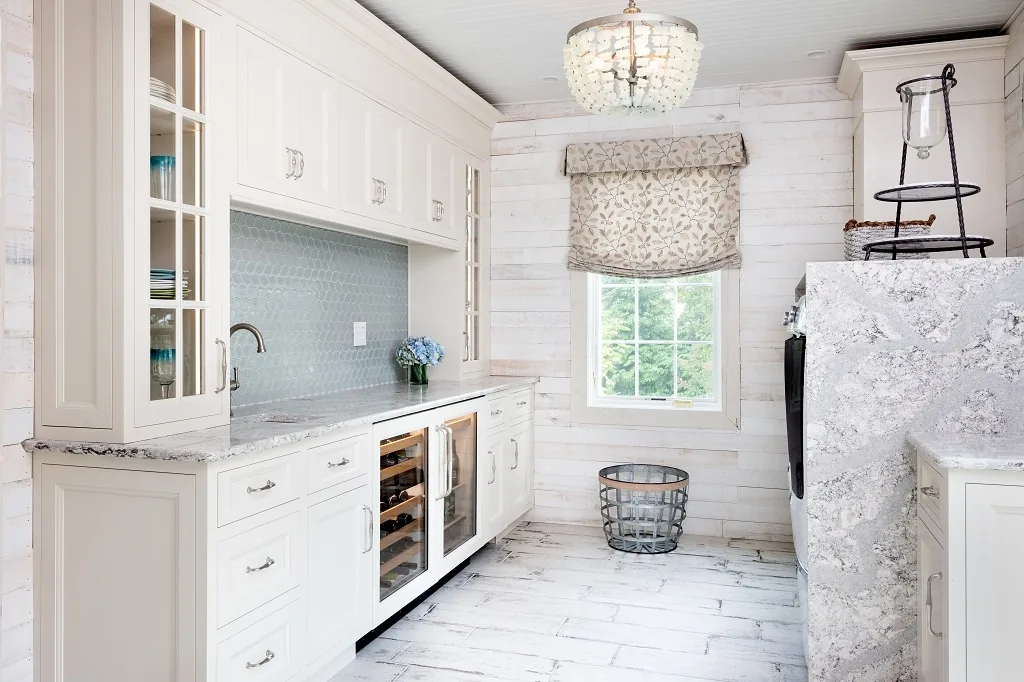 Churchville beverage center after renovation with white glass-front cabinetry, a blue hexagon glass tile backsplash, a marble counter, a built-in wine and beverage fridge, a beaded chandelier, and shiplap walls