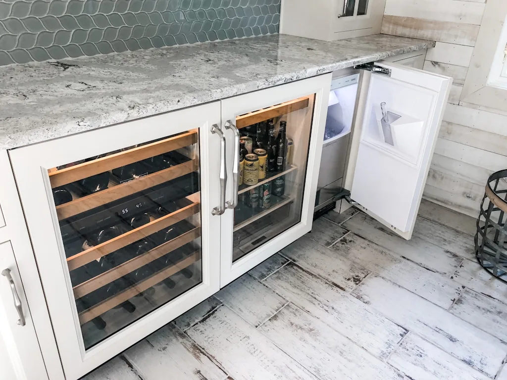 Open built-in wine and beverage refrigerator with wood racks under a marble counter and blue hexagon tile in the Churchville kitchen beverage center