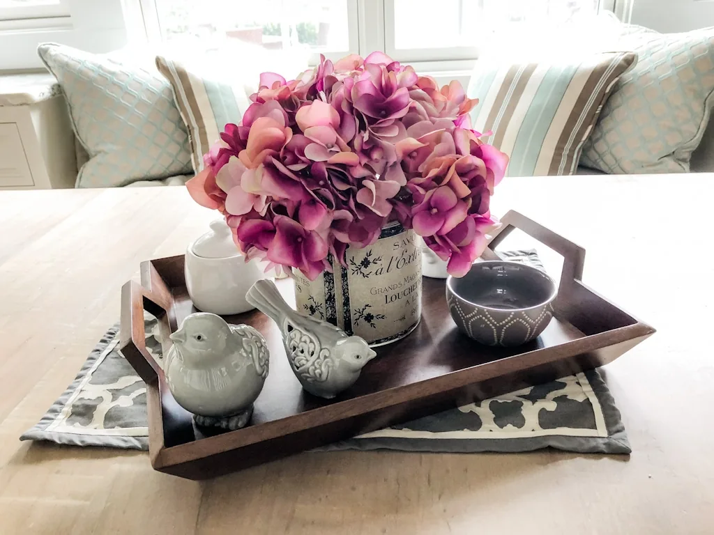 Styled breakfast-nook vignette with pink hydrangeas in a French label vase, ceramic birds, and a sugar pot on a dark wood tray in the Churchville kitchen