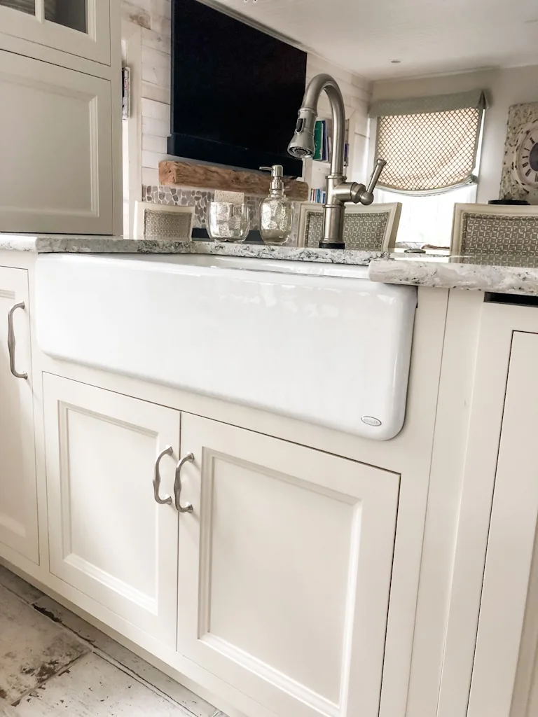 White farmhouse apron-front sink with a brushed-nickel faucet beneath white cabinetry and a granite counter in the Churchville kitchen