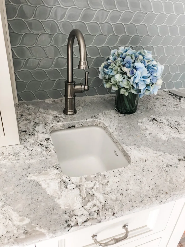 Square undermount prep sink with a brushed-nickel gooseneck faucet, blue hydrangeas, and a blue hexagon glass tile backsplash on a granite island in the Churchville kitchen