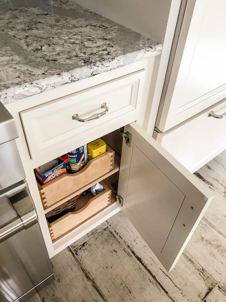 Two-tier dovetailed wood pull-out drawers behind a cabinet door storing pantry goods beneath a speckled granite counter in the Churchville kitchen