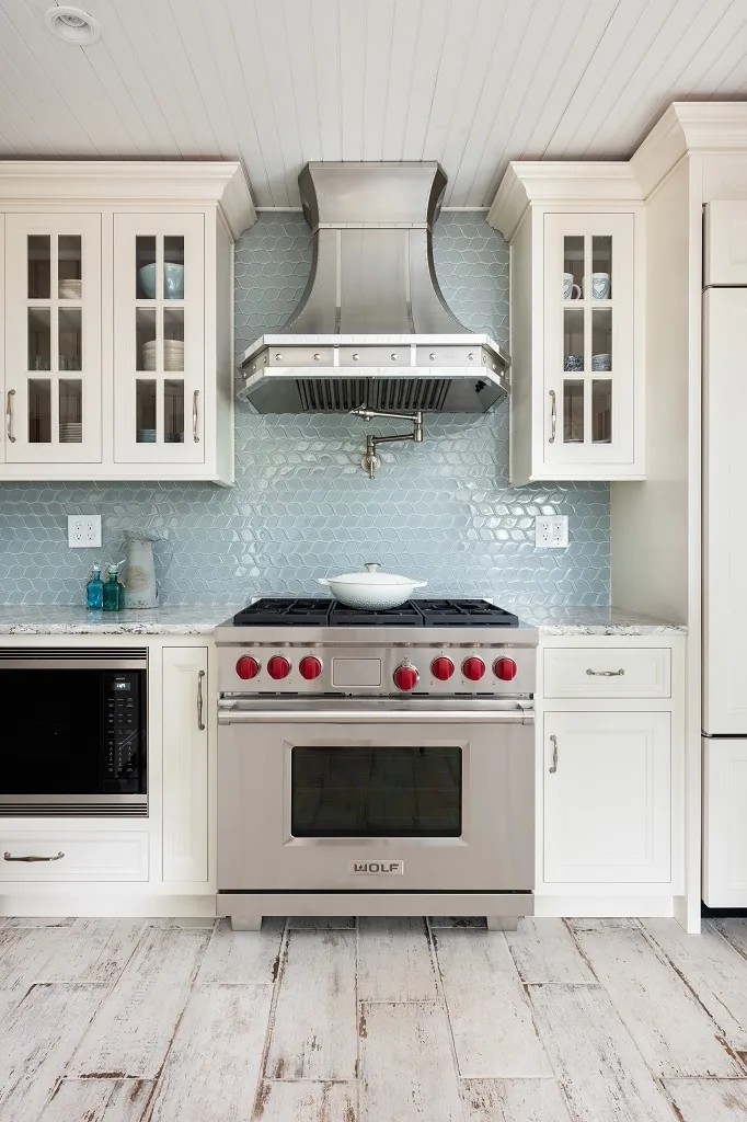Stainless Wolf range with red knobs beneath a curved stainless hood and blue hexagon glass tile, flanked by glass-front cabinets in the Churchville kitchen