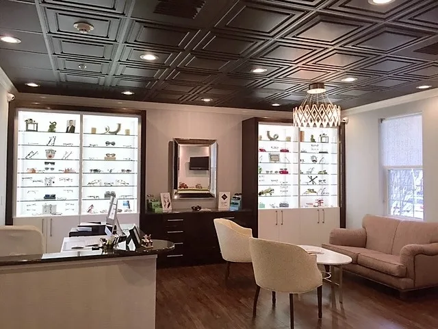 Boutique optometry reception and dispensing area with coffered black ceiling, chandelier, and backlit eyewear display cabinetry