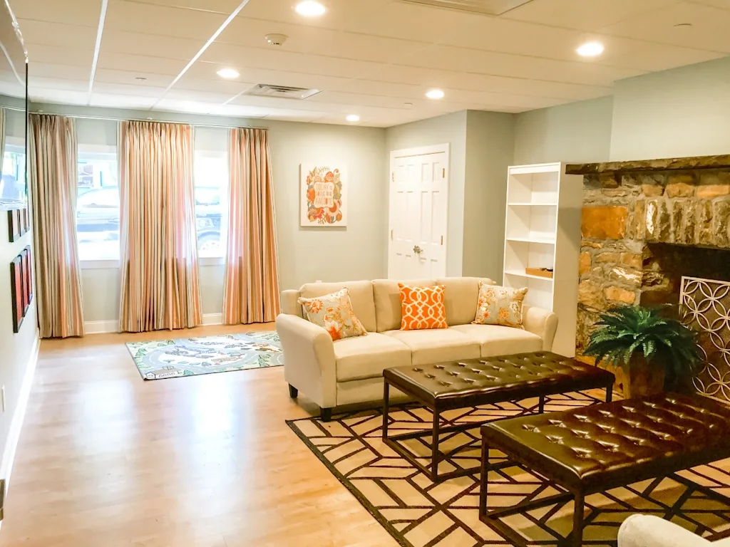 Cozy living room with stone fireplace and cream sofas in a residential healthcare facility designed by NGD Interiors