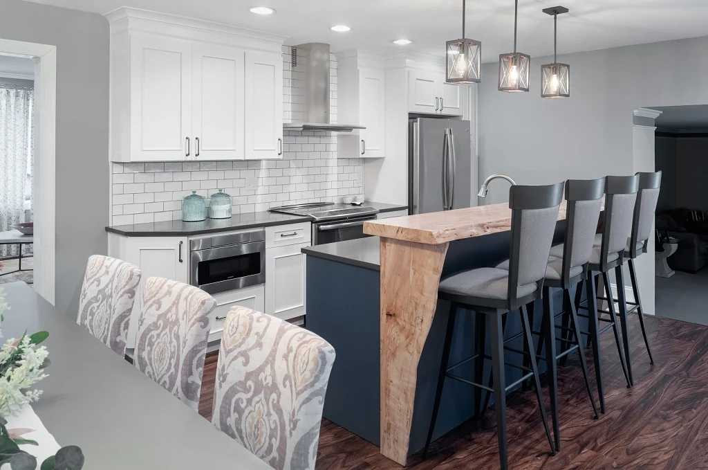 Holland mix and match kitchen after renovation with crisp white shaker perimeter cabinets, a navy island topped by a live-edge waterfall wood bar, dark quartz countertops, a white subway tile backsplash, stainless steel appliances, geometric pendant lights, and dark walnut floors