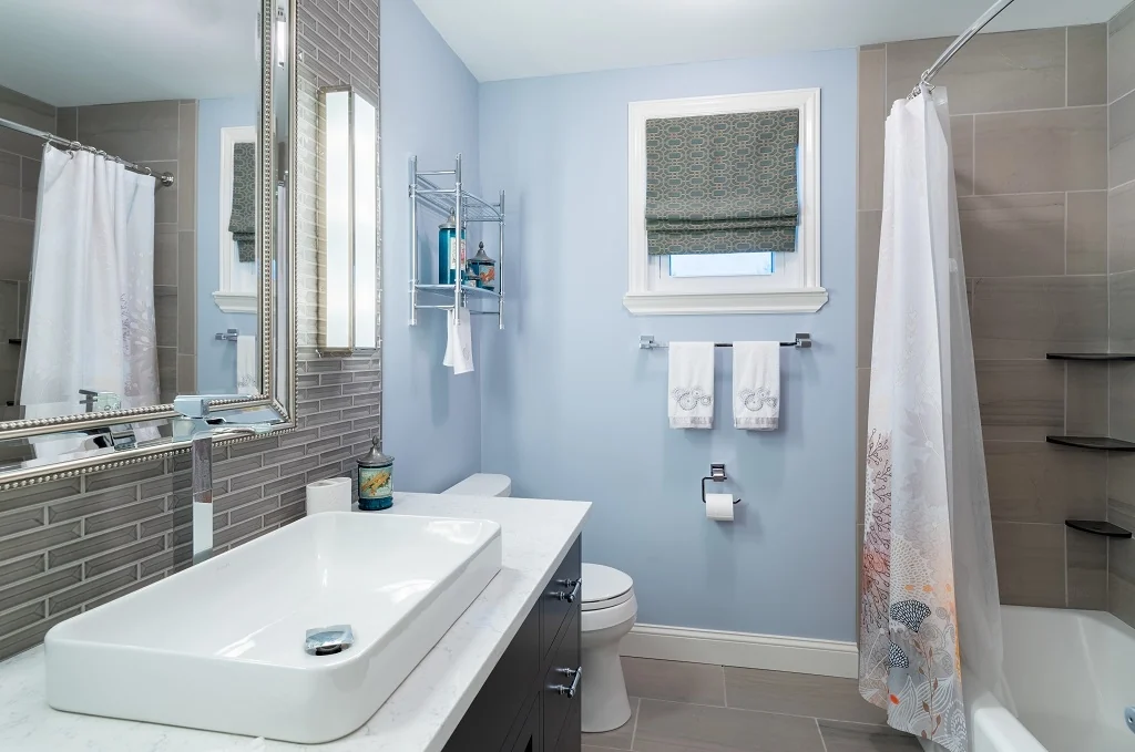 Holland contemporary bathroom after renovation with a custom navy Nina Green Signature Series vanity, white quartz countertop and vessel sink, a shimmering linear glass tile accent wall, a beaded silver mirror, soft blue walls, and a porcelain-tiled tub and shower