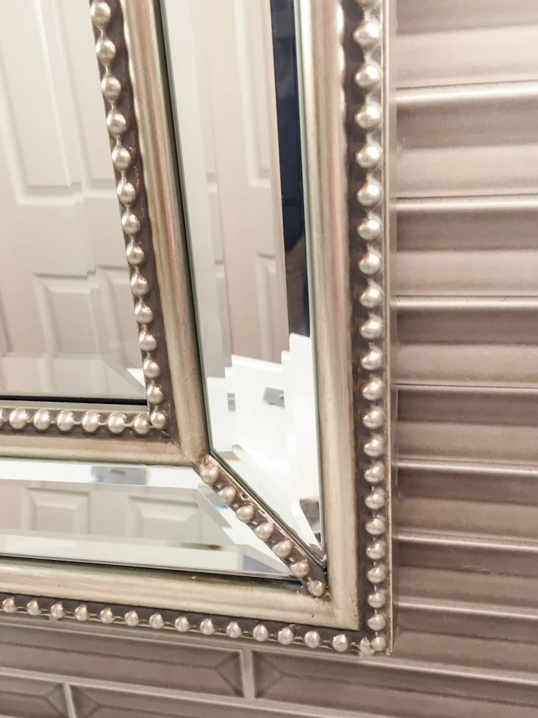Close-up of the beaded silver mirror frame against the shimmering linear glass tile accent wall in the Holland contemporary bathroom