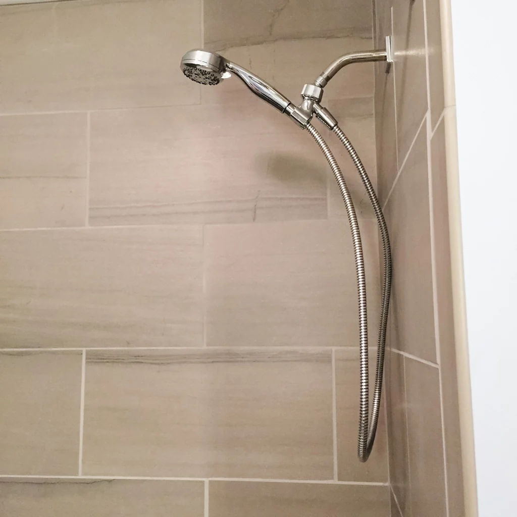 Brushed-nickel handheld shower head on a slide arm against the large-format wood-look porcelain shower wall in the Holland contemporary bathroom