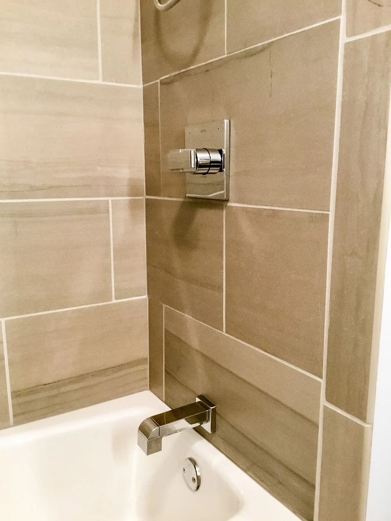 Modern square chrome tub spout and single-handle shower valve set into the large-format porcelain tub surround in the Holland contemporary bathroom