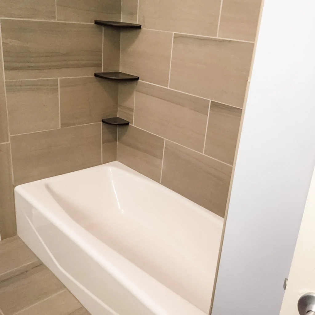 White tub with large-format wood-look porcelain wall tile and three floating dark corner shelves in the Holland contemporary bathroom