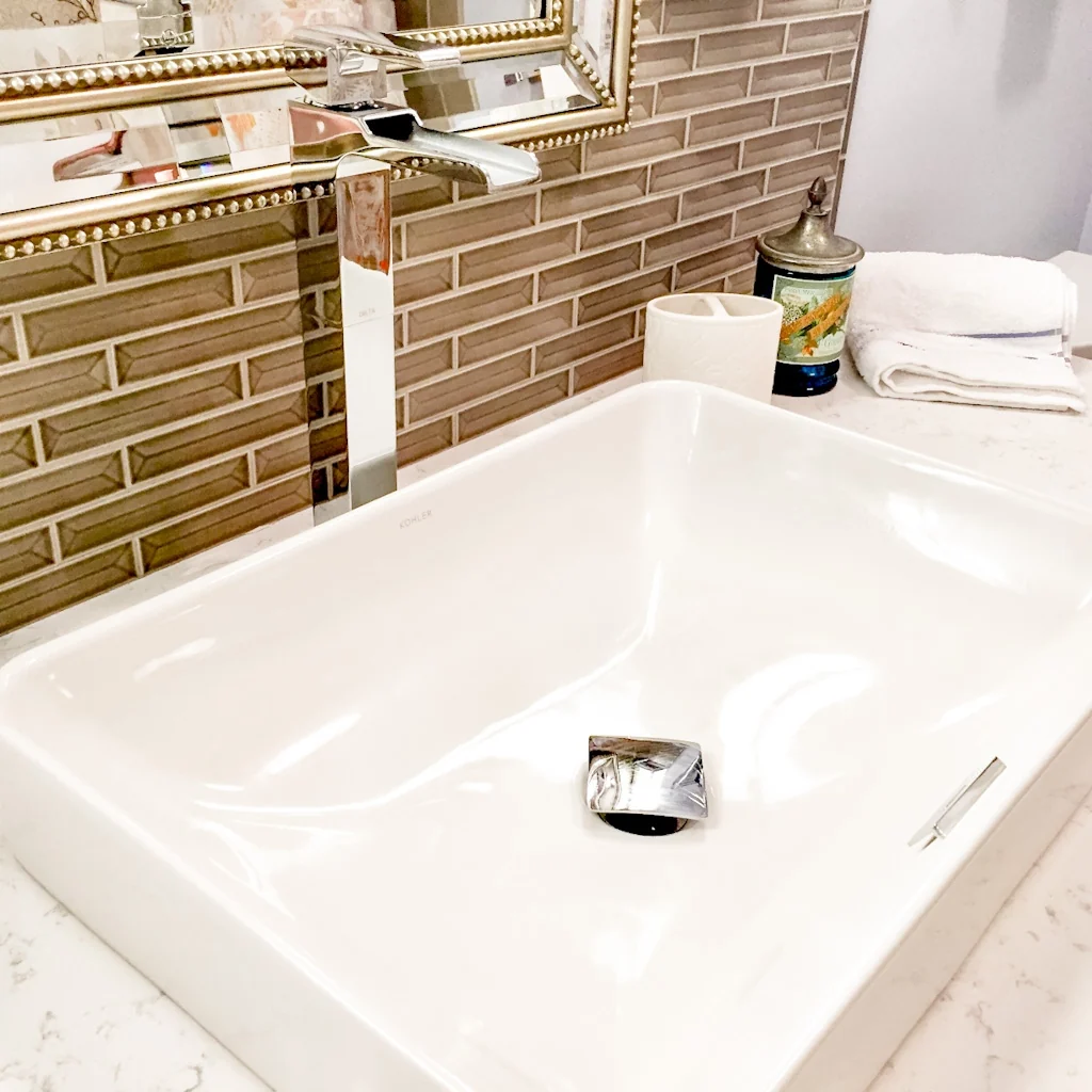 Close-up of the rectangular Kohler vessel sink and polished chrome waterfall faucet on the white quartz vanity top against the shimmering linear glass tile wall in the Holland contemporary bathroom