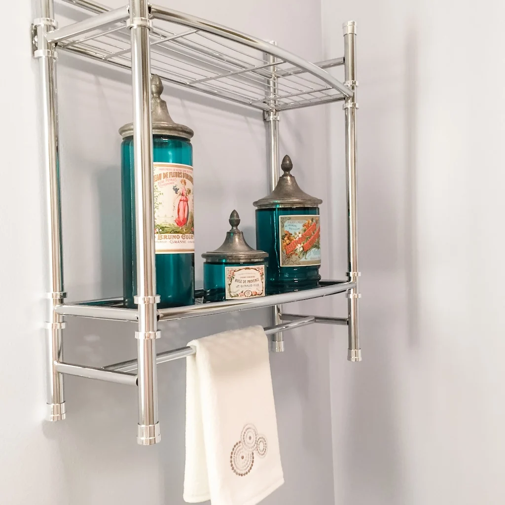 Polished chrome wall shelf unit with teal apothecary jars and a monogrammed white hand towel in the Holland contemporary bathroom