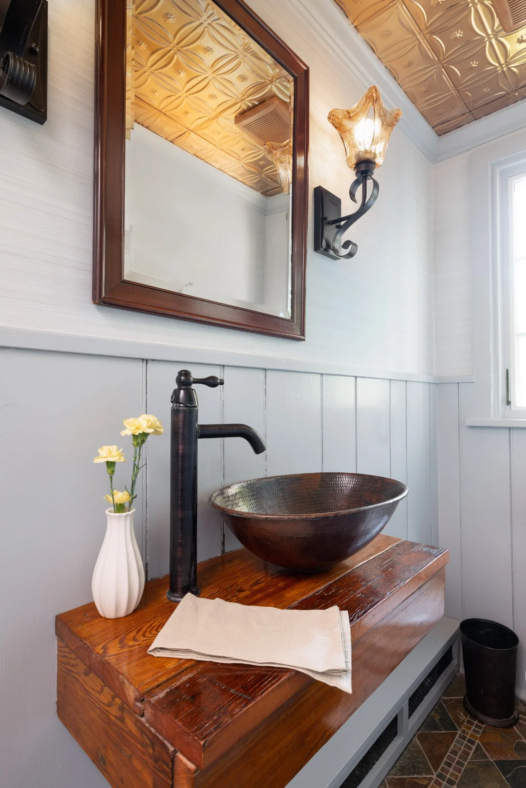 Richboro powder room vanity with a hammered-copper vessel sink on a reclaimed-wood floating shelf, an oil-rubbed-bronze faucet and sconce, a wood-framed mirror, and a pressed-copper tin ceiling