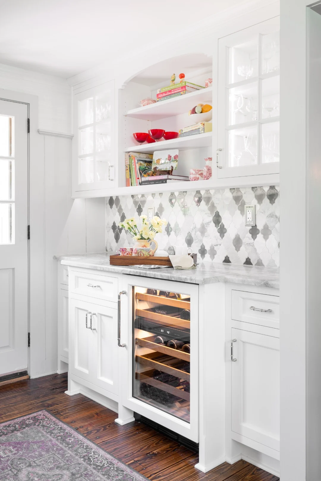 Built-in white hutch in the Richboro kitchen with glass-front upper cabinets, open arched display shelving, a marble counter, arabesque backsplash, and an integrated wine refrigerator beside the back door