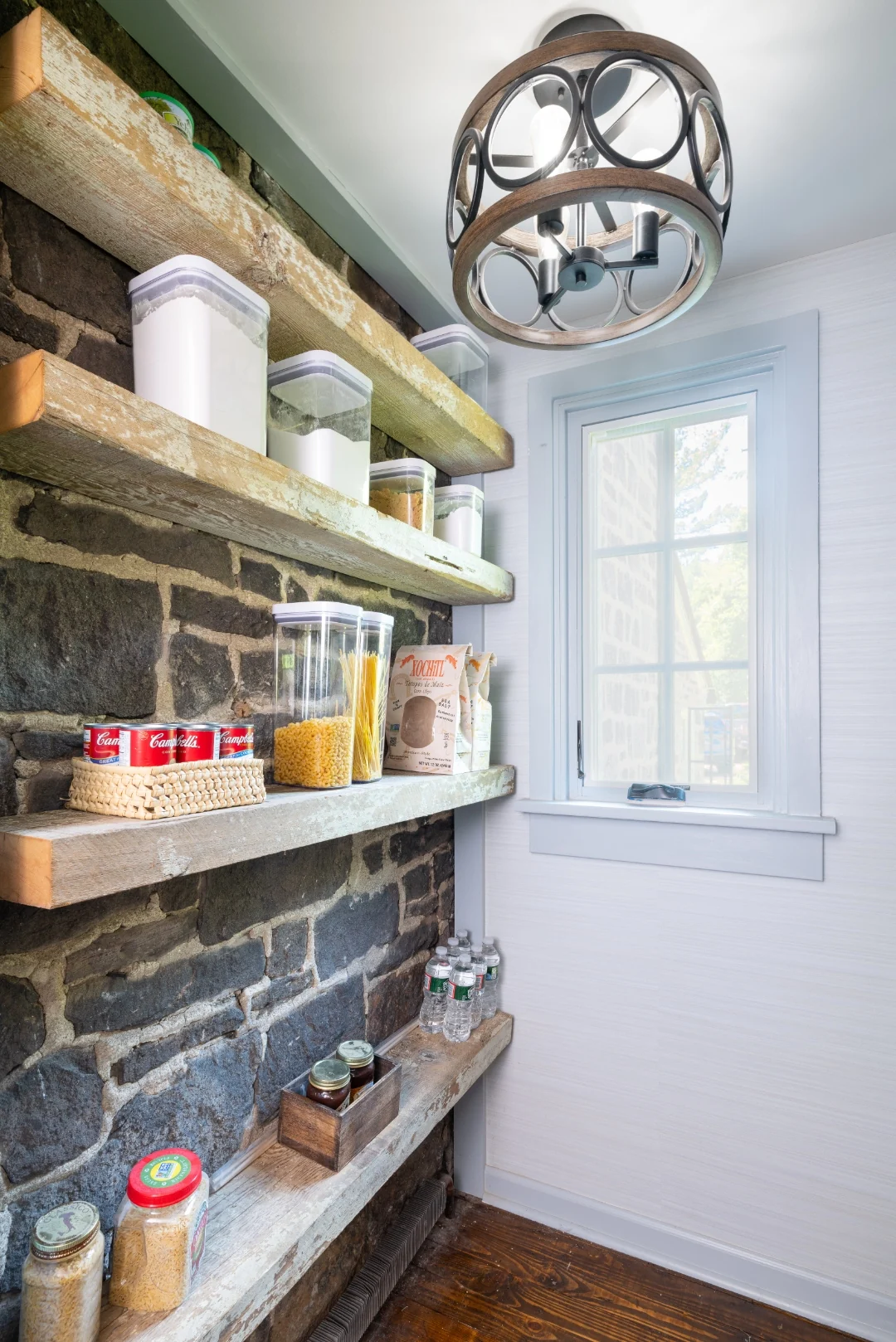 Detail of the Richboro pantry exposed stone wall with thick reclaimed-wood floating shelves holding canisters and pantry staples beside a trimmed window