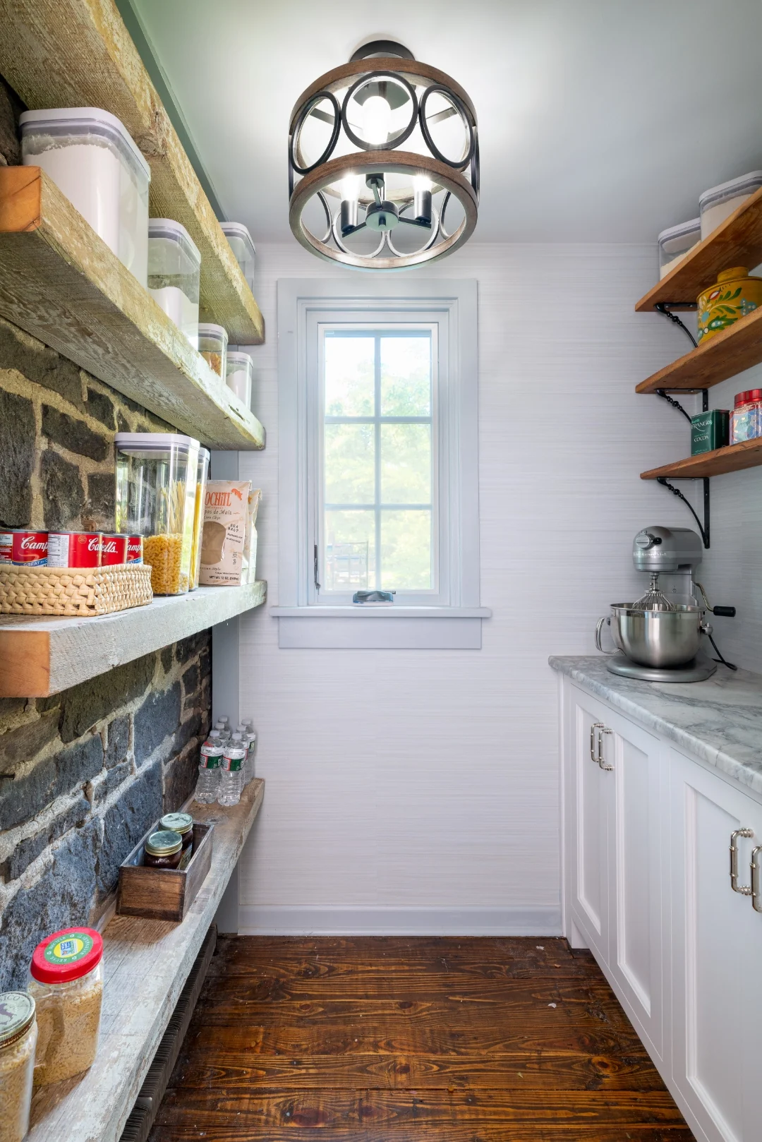 Richboro rustic pantry with an exposed natural stone wall, reclaimed-wood floating shelves stocked with provisions, a window, and a white base cabinet with a marble counter and stand mixer