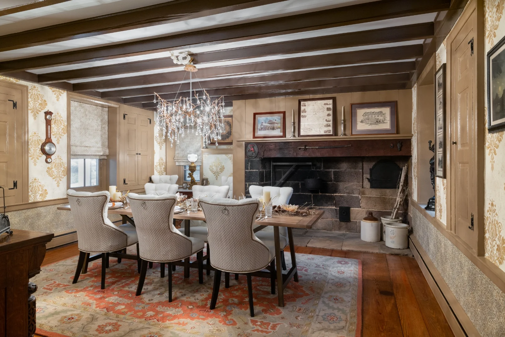 Wide view of the Southampton dining room showing the trestle table, white wingback dining chairs, layered Oushak rug, and the restored stone walk-in hearth beneath painted beams