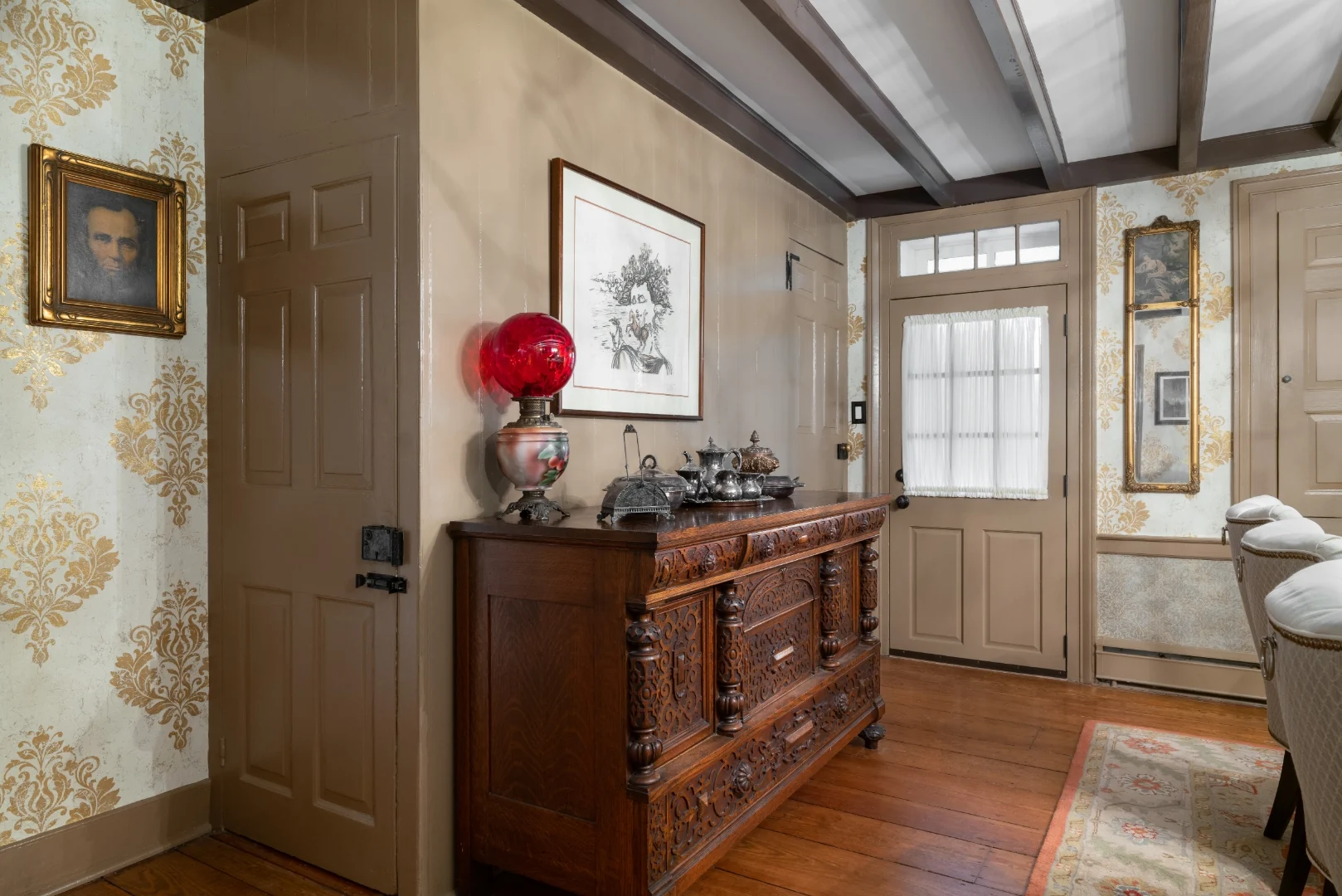 Carved oak Victorian sideboard with an antique red-globe oil lamp and silver tea service against gold damask wallpaper and a portrait of Lincoln in the Southampton dining room
