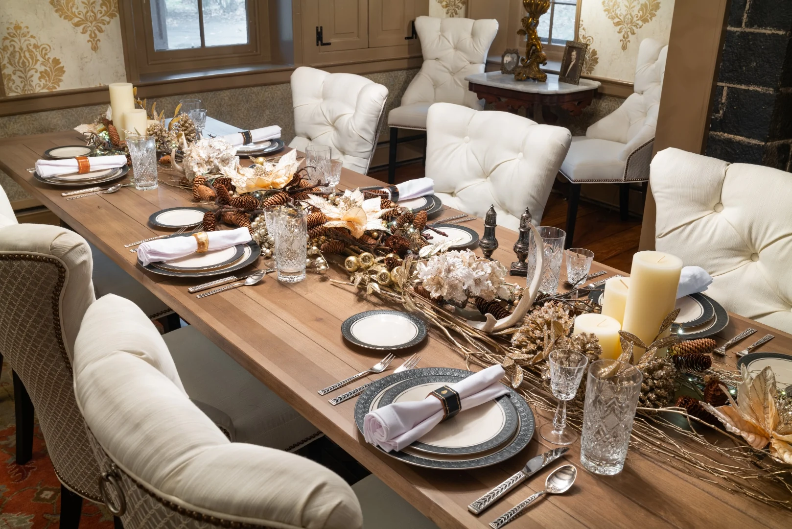 Holiday tablescape detail with gilded chargers, crystal stemware, white poinsettias, pinecones, antlers, and pillar candles along the trestle table in the Southampton dining room