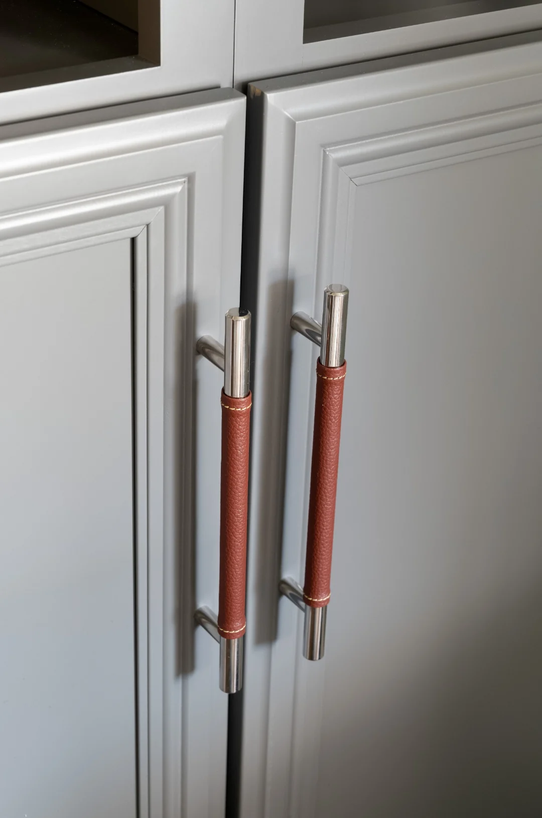 Detail of custom gray built-in cabinet doors with polished-nickel and saddle-leather wrapped pull hardware in the Yardley transitional rustic living room