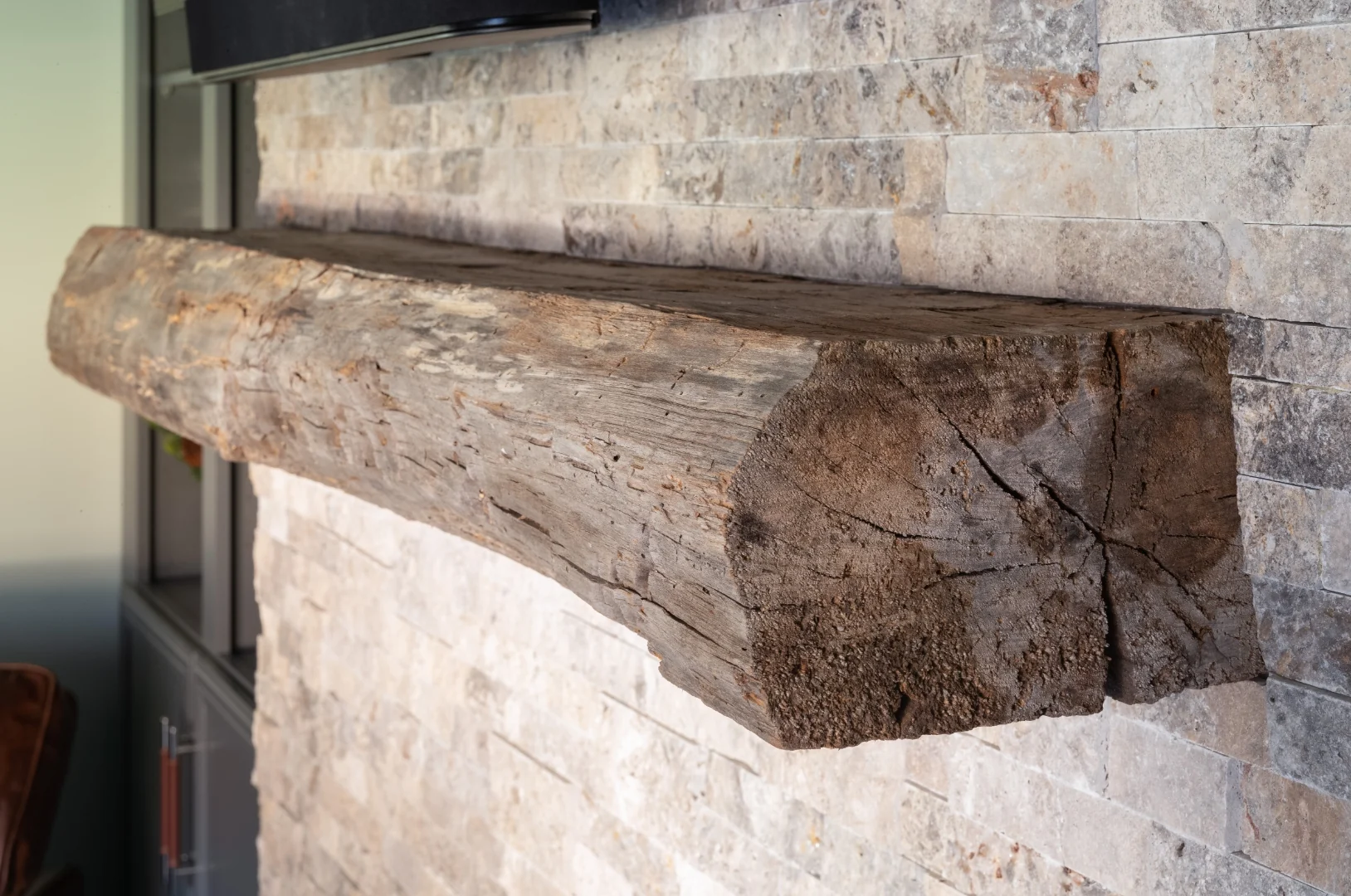 Close-up of the rough-hewn reclaimed wood mantel beam set into the stacked stone fireplace surround in the Yardley transitional rustic living room